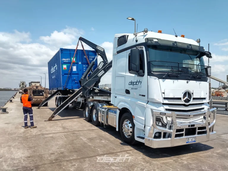 Depth Logistics Mercedes-Benz prime mover with sideloader lifting a blue container, worker in hi-vis nearby